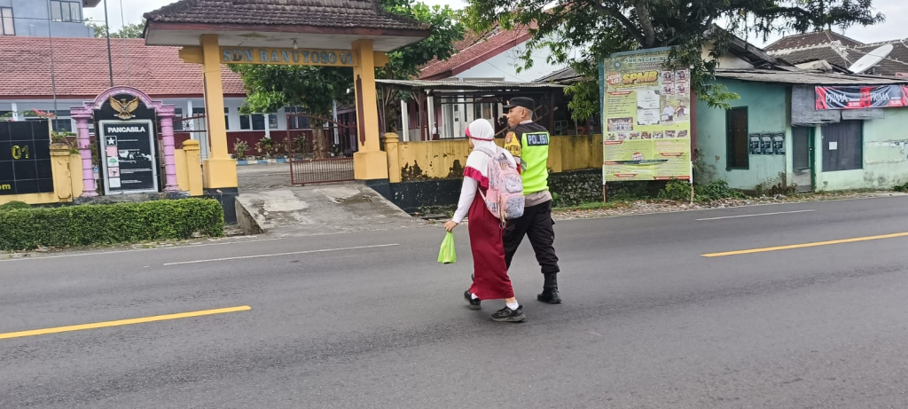 Personel Polsek Ranuyoso membantu pelajar menyeberang dan mengatur arus lalu lintas di hari pertama masuk sekolah melalui program Polisi Ketok.